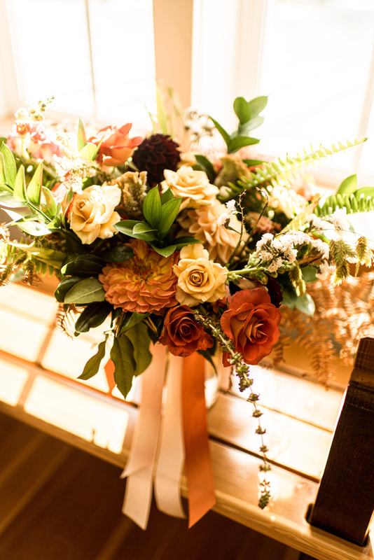 vibrant orange bridal bouquet with ferns sits on windowsill 