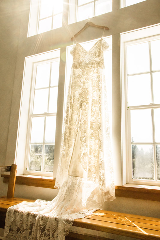 grace loves lace bridal gown hanging in a large window while the sun shines through