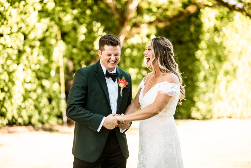 groom in green jacket and bride in grace loves lace dress laugh as they hold hands