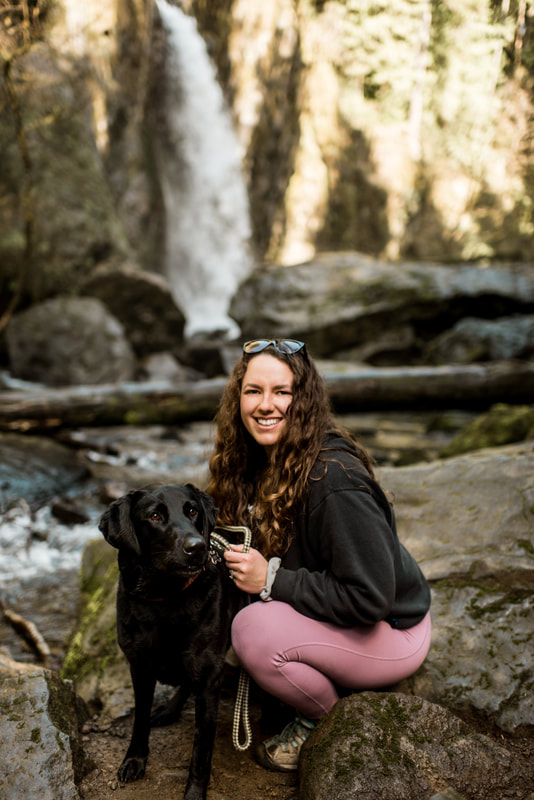 waterfall elopement photographer sits next to her black lab in front of Drift Creek Falls in Oregon.