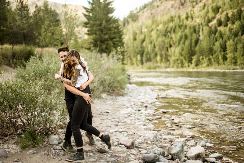 engaged couple laugh together as they walk along the Flathead River in Montana